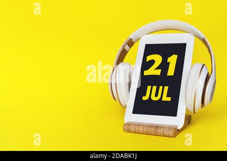 July 21st . Day 21 of month, Calendar date. Stylish headphones and modern tablet on yellow background. Space for text. Education, technology, lifestyl Stock Photo