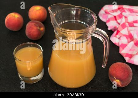 Peach juice in a jug and ripe peaches on a black background. Stock Photo