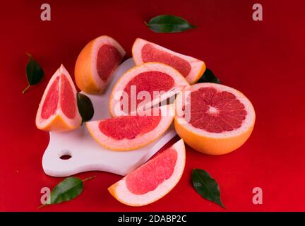 Sliced ​​grapefruit on a white wooden board on a red background. Stock Photo