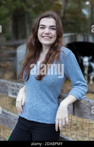 Portrait ot pretty teenage girl smiling at goat pen in farm setting Stock Photo