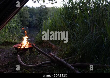 Corner of boho hammock next to lake and fire in fire pit at dusk at romantic campsite atmosphere Stock Photo