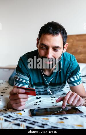 Man shopping online on a tablet lying on the bed at home Stock Photo