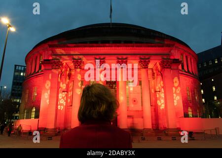 Armistice Day Commemoration during lockdown. Manchester Central Library, UK lit with red light and poppy design. Woman looking on. St Peter's Square Stock Photo