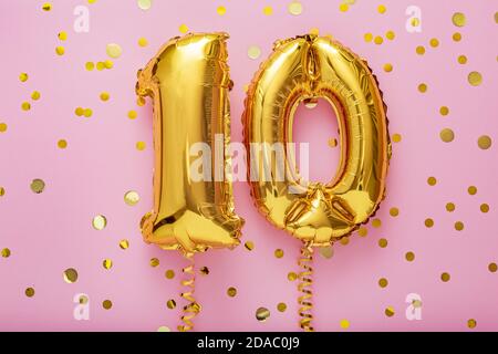 10 air balloon numbers on pink background. 10 k gold foil balloons with confetti. Birthday party flat lay with copy space Stock Photo