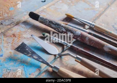 Various brushes & pallete knives .The wooden desk is covered with beautiful different coloured paints. Stock Photo
