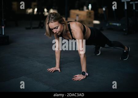Fitness young woman with perfect athletic body wearing black sportswear doing push-ups exercise Stock Photo
