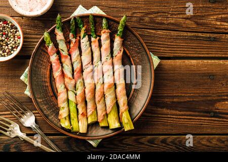 Asparagus shoots baked in bacon. Snack on wooden background Stock Photo