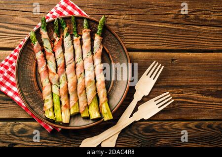 Asparagus shoots baked in bacon. Snack on wooden background Stock Photo