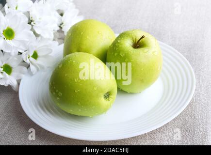 Three washed green apples "Golden" on a white plate and chrysanthemums Stock Photo