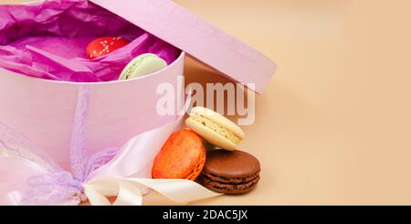Four brightly colored French Macarons with pink cardboard box on peach background. Stock Photo