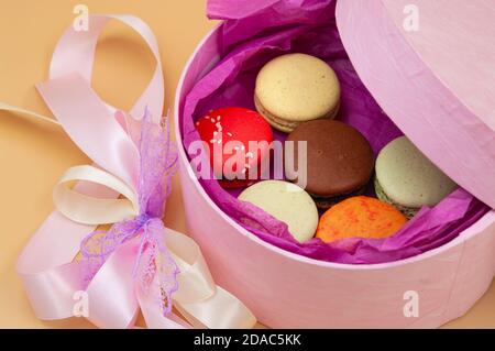 Four brightly colored French Macarons in pink cardboard box on peach background Stock Photo