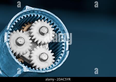 White planet gears inside a ring cogwheel of epicyclic gear train on a blue background. Plastic and metallic cog wheels.in electric screw gun gearbox. Stock Photo