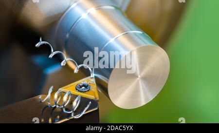 Closeup of turning cylindrical workpiece of aluminum alloy on lathe machine. Black cutting tool bit with yellow triangular carbide insert. metal swarf. Stock Photo