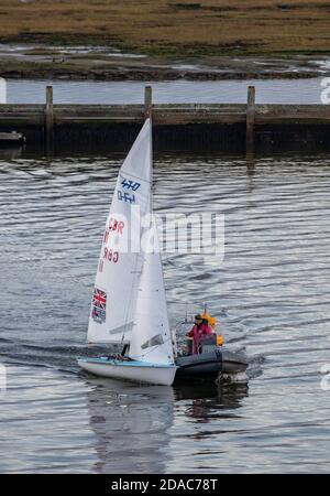 a small racing dinghy being towed into lymington marina by a rib after having become becalmed with now ind on a calm day. Stock Photo