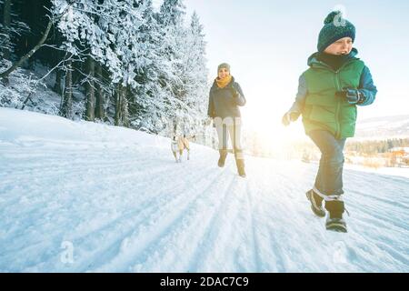 Mother and son having a fun. They running with their beagle dog in snowy forest during dog walk. Mother and son relatives and femily values concept im Stock Photo