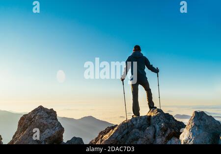 Young hiker Man standing with trekking poles on a cliff edge and looking at Tatra mountains valley covered with clouds. Successful Velky Rozsutec 1610 Stock Photo