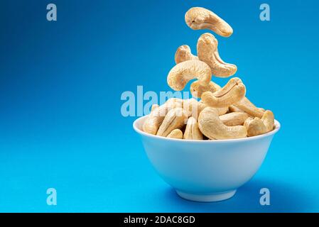 Falling cashew nuts into bowl on blue background Stock Photo