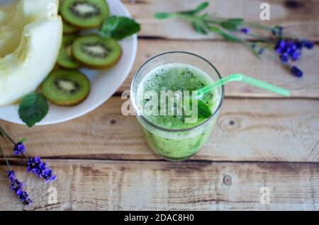 Glass of fresh home made smoothie with kiwi, melon and mint and plate with fruits used as ingredients on rustic wooden table Stock Photo
