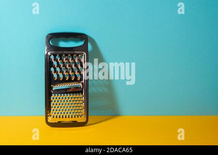 Stainless steel grater with plastic handle on yellow and blue background Stock Photo