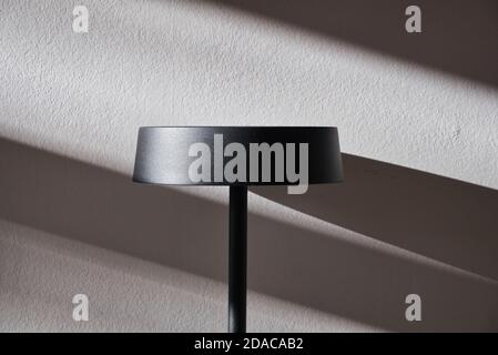 Metal lampshade on white wall with daylight and shadows. Stock Photo