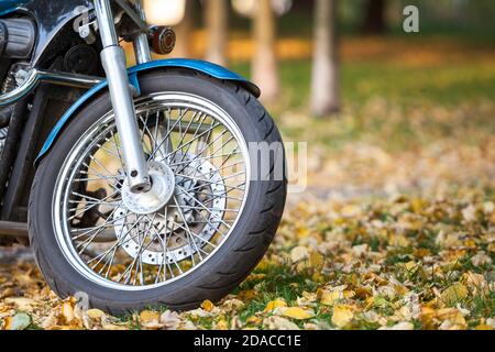 Wire-spoked wheel of a classic motorcycle standing on yellow leaves in autumn park, copyspace Stock Photo