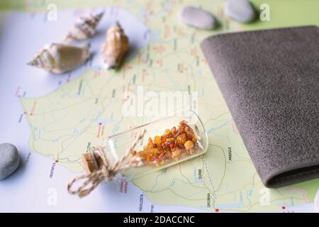 Miniature glass jar with amber, passport in a leather cover, some stones and sea shells are lying on a map of Latvia (fragment). Stock Photo