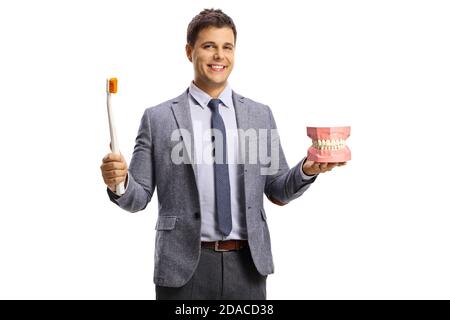 Young man in a suit and tie showing a jaw model and a big toothbrush isolated on white background Stock Photo