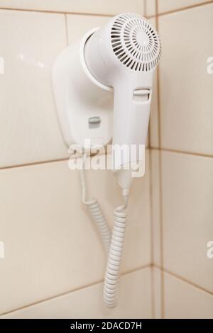 White hair dryer hanging on wall in a bathroom Stock Photo