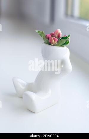 White ceramic figurine of human with apple flower buds on his head is sitting on a window sill Stock Photo