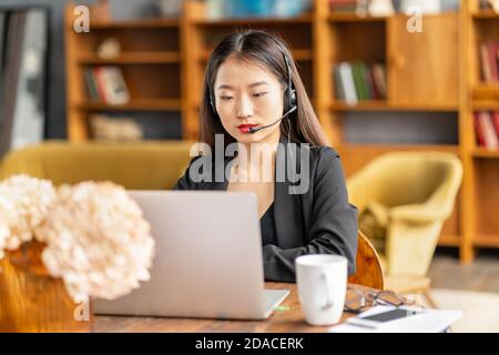 Asian businesswoman in headset speaking by conference call and video chat Stock Photo