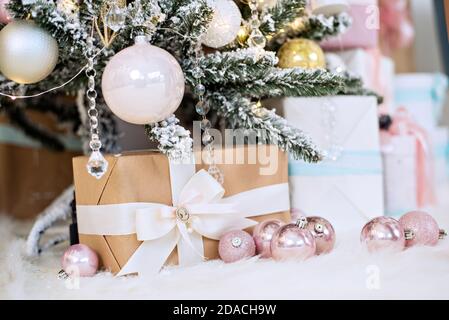 New Year greeting card. Craf boxes with gifts from Santa Claus lie on white fur under a snowy Christmas   tree decorated with glass toys, pink balls Stock Photo