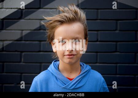 Funny portrait of a blonde caucasian boy whose hair rises and flies in the wind. Looks at the camera Stock Photo