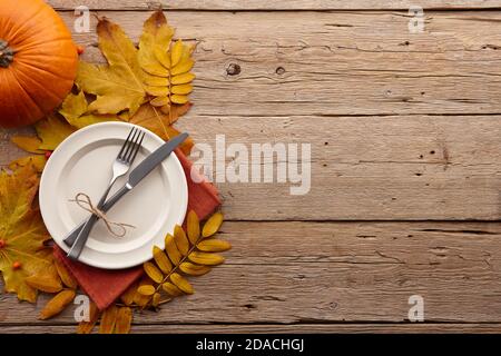 Thanksgiving dinner concept. Autumn leaves, pumpkins and plate with cutlery on wooden rustic table. Stock Photo