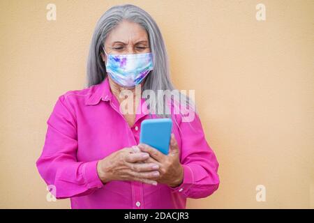 Senior woman using mobile phone while wearing protective face mask - Focus on face Stock Photo