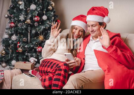 Portrait of lovely couple husband and wife in red Santa hat having a video call or taking selfie with their smartphone, enjoy Christmas time at home Stock Photo