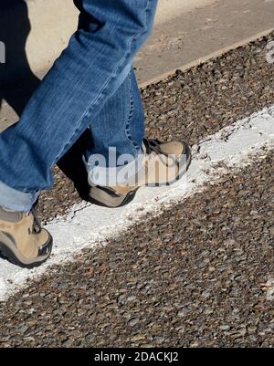 A woman tests her balance by walking down a white line painted along the edge of a road, similar to a sobriety test administered by police. Stock Photo