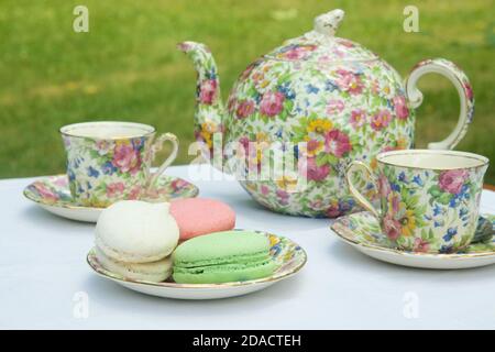 Floral china teapot, teacups, and plated macaroons. Stock Photo