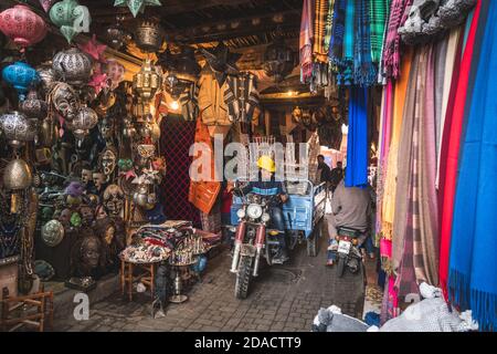 Marrakech, Morocco - APRIL 26 2019: Citizen on a motorcycle and view of the shops on a busy street in Medina Stock Photo