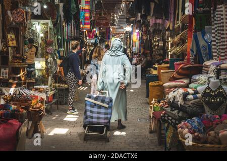 Marrakech, Morocco - APRIL 26 2019: Citizen woman dressed in arabic clothes walking on a busy crowded street in Medina Stock Photo