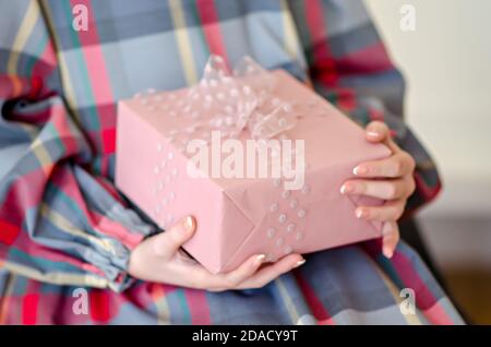 The hands of a girl in a checkered dress are holding an elegant, delicate pink gift with an airy, transparent polka dot ribbon. New year greeting card Stock Photo