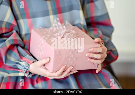 The hands of a girl in a checkered dress are holding an elegant, delicate pink gift with an airy, transparent polka dot ribbon. New year greeting card Stock Photo