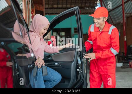 The mechanic in red uniform opens the car door when the customer comes to repair the car at the garage Stock Photo