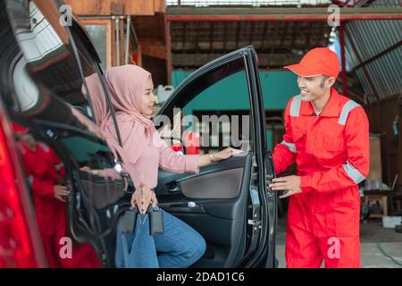The mechanic in the red uniform closes the customer's door after the car is repaired in the garage Stock Photo