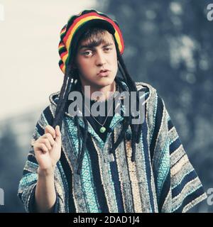 Sad young fashion hipster man walking outdoor Stylish trendy model in rasta hat and poncho Stock Photo