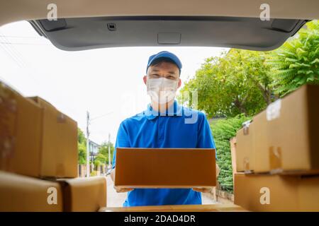 Asian Delivery man services courier working with cardboard boxes on van during the Coronavirus (COVID-19) pandemic, courier wearing medical mask and l Stock Photo