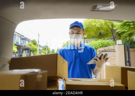 Asian Delivery man services courier working with cardboard boxes on van during the Coronavirus (COVID-19) pandemic, courier wearing medical mask and l Stock Photo