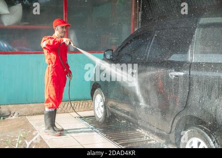 Asian male car cleaner wearing red uniform sprays water while washing the car in the car salon Stock Photo