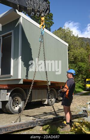 GREYMOUTH, NEW ZEALAND, OCTOBER 21, 2020: A crane operator works on lifting a small building from a truck onto its pilings. Stock Photo
