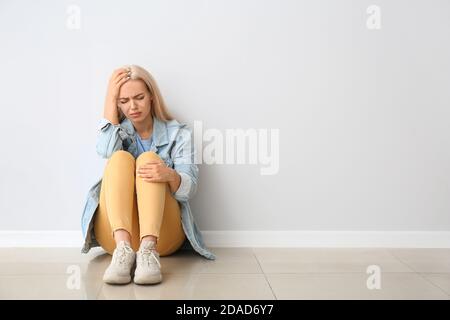 Stressed young woman sitting near light wall Stock Photo