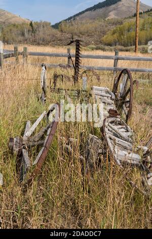 A broken-down old pioneer wagon with wooden-spoke wheels and a vintage sicklebar hay mower on a ranch in Idaho.  Now part of a private museum. Stock Photo